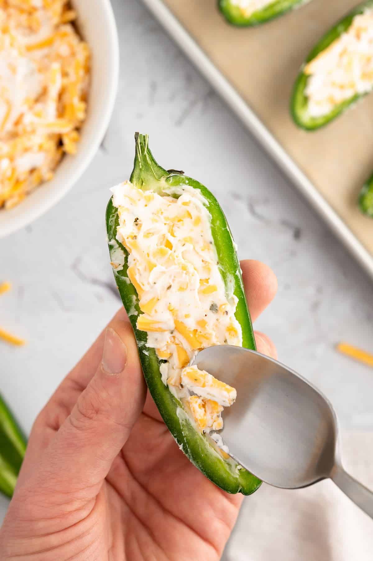 A halved jalapeno pepper being filled with vegan cheeses to create a jalapeno popper.