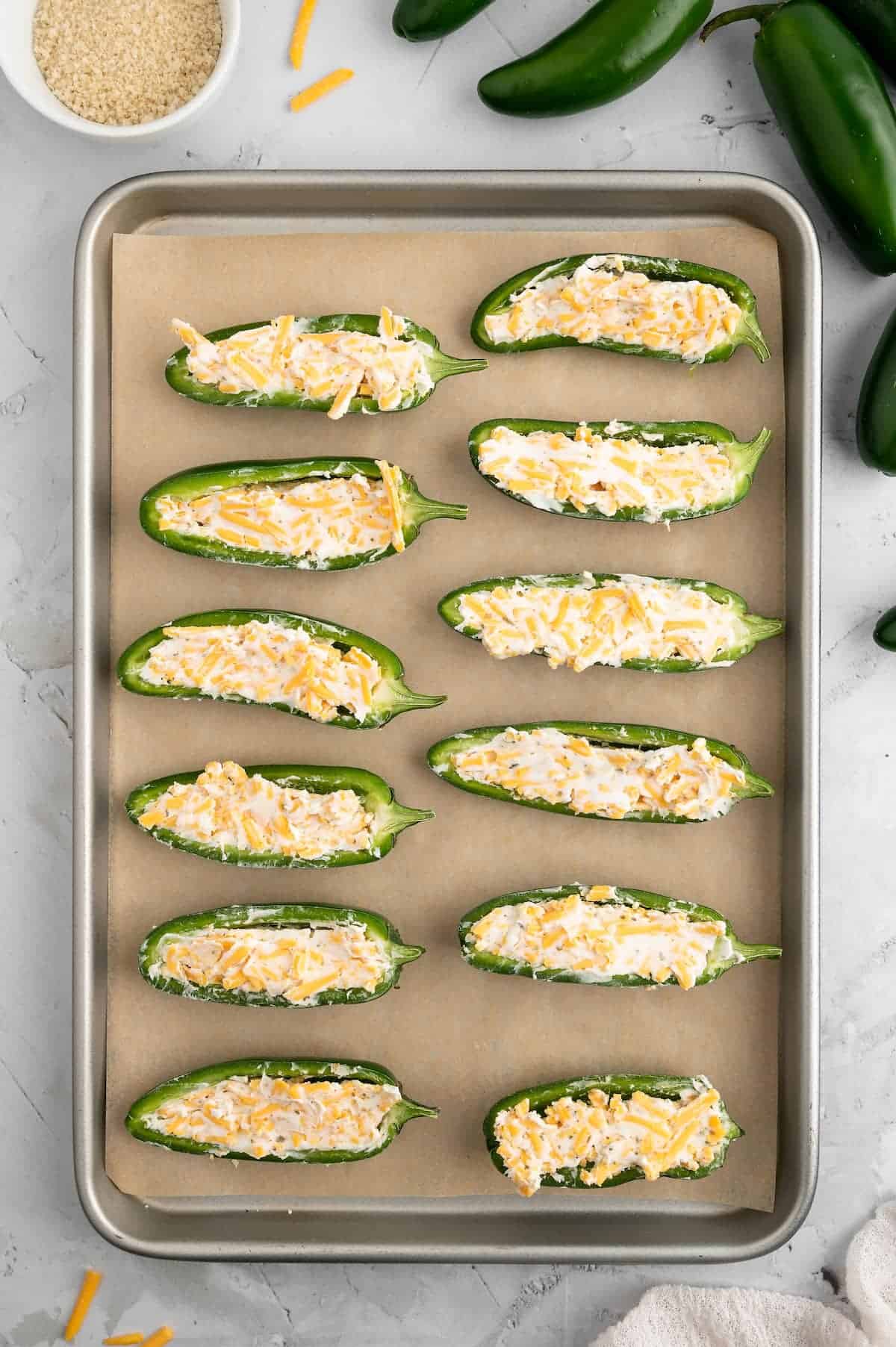 Jalapeno poppers filled with a vegan cheese mixture and lined up on a baking sheet.