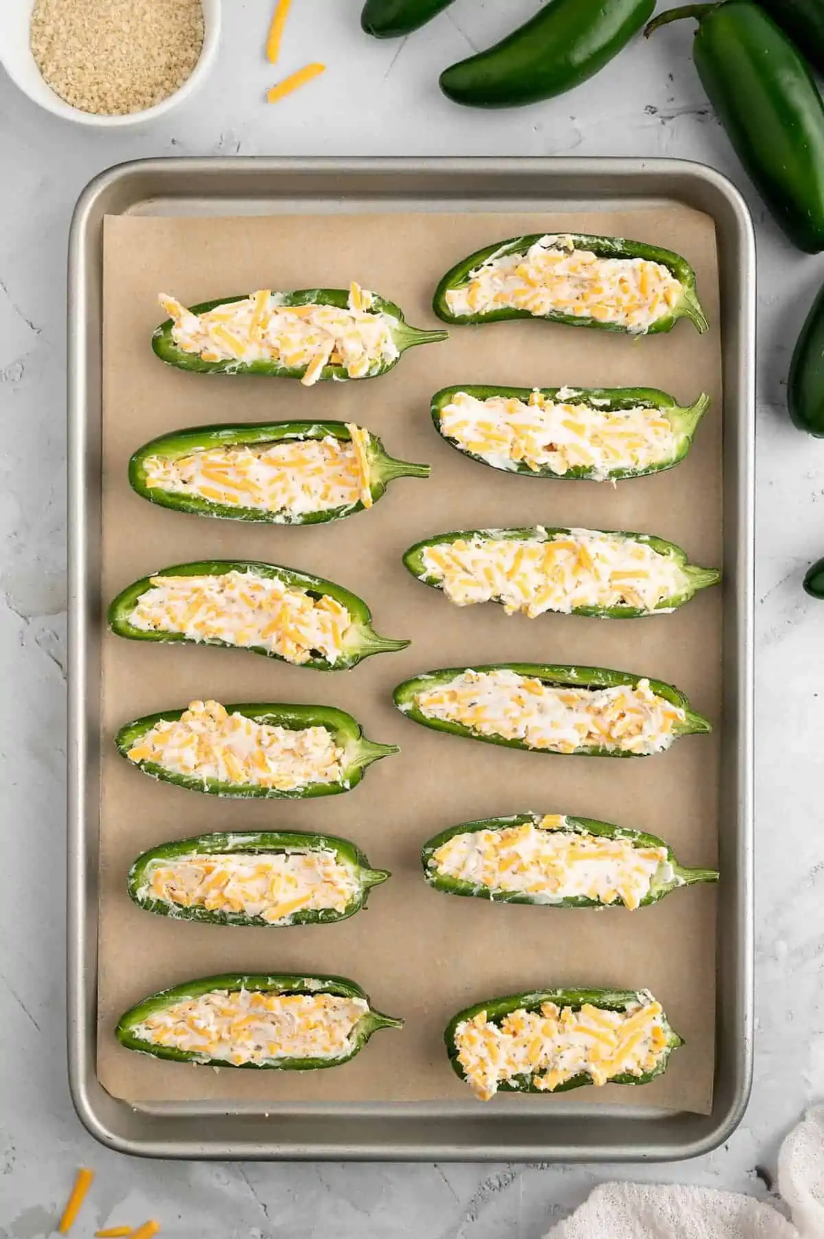 Jalapeno poppers filled with a vegan cheese mixture and lined up on a baking sheet.