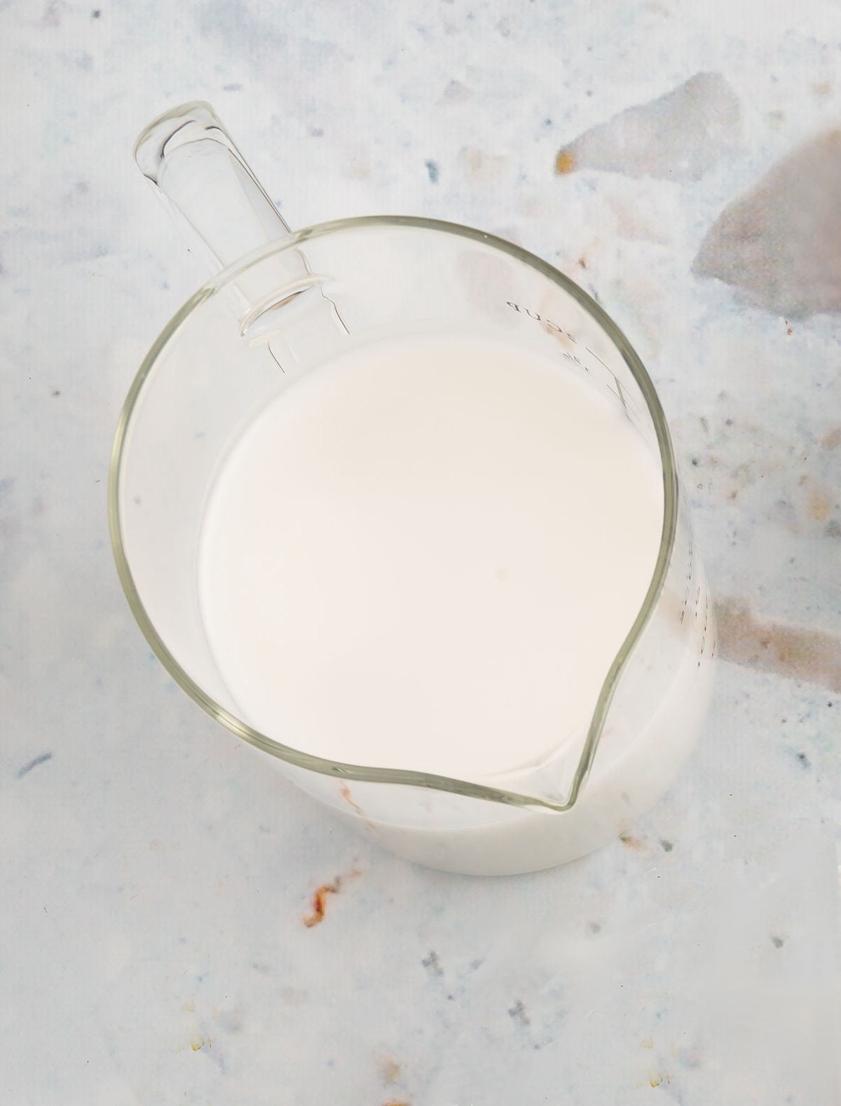 A glass measuring cup for fluid ounces and cups filled with non-dairy milk.