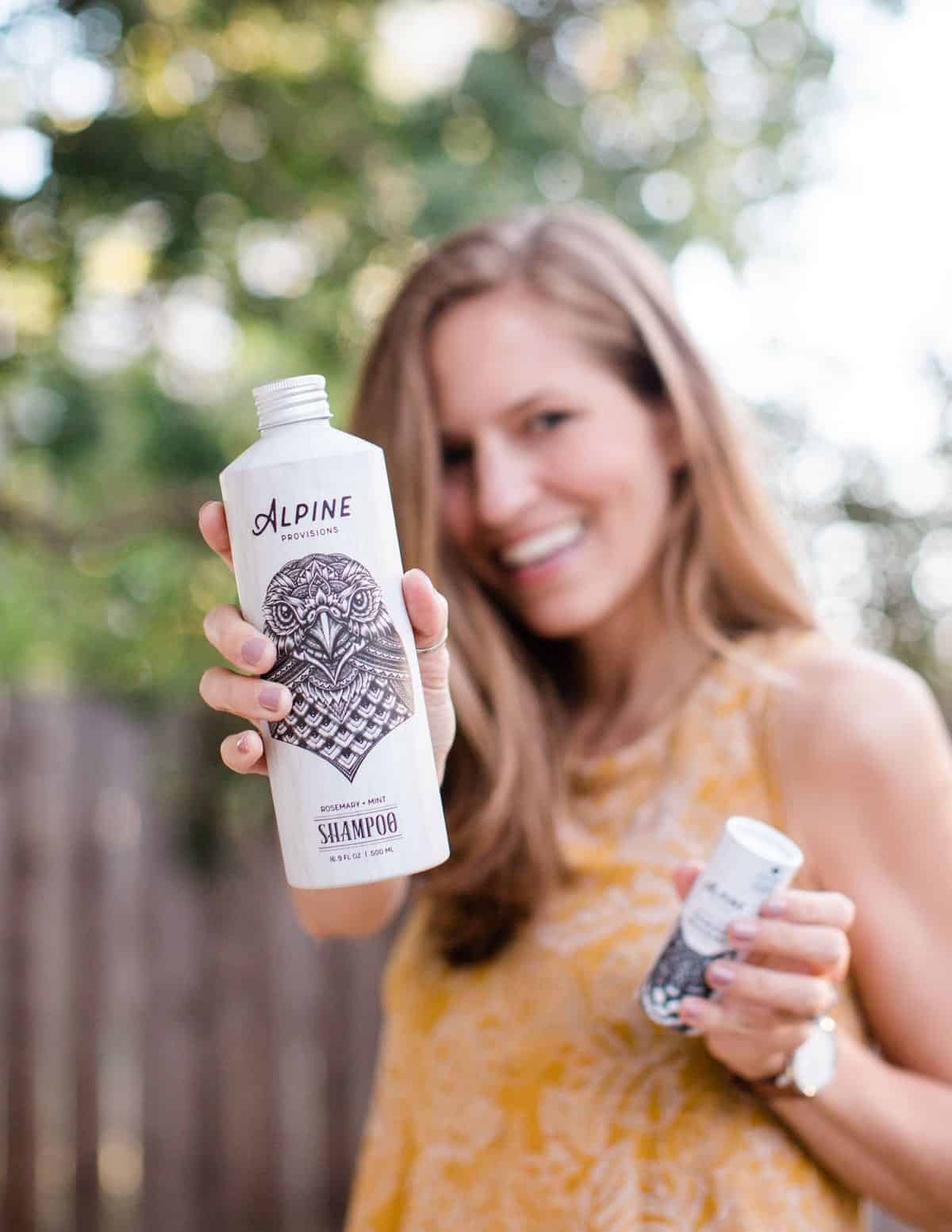 Michelle Cehn holding out a bottle of Alpine Provisions vegan shampoo and conditioner. 