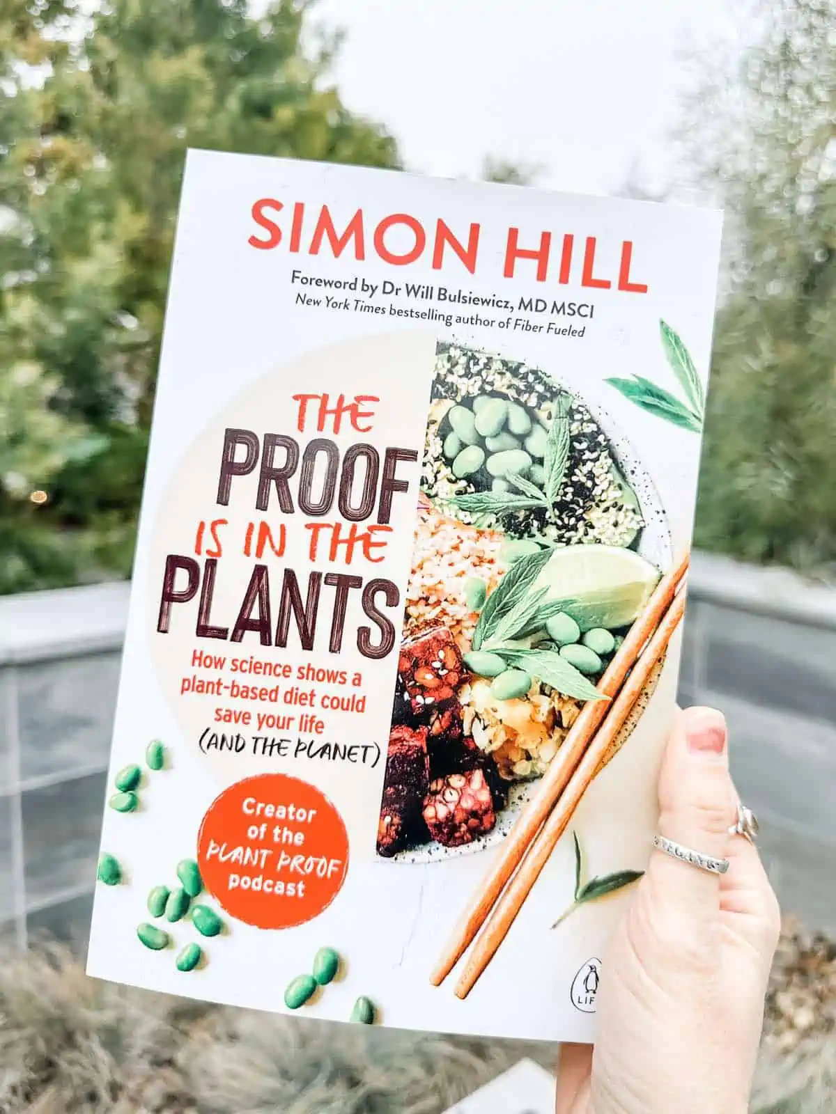 Vegan holding out Simon Hill's book The Proof is in the Plants. 