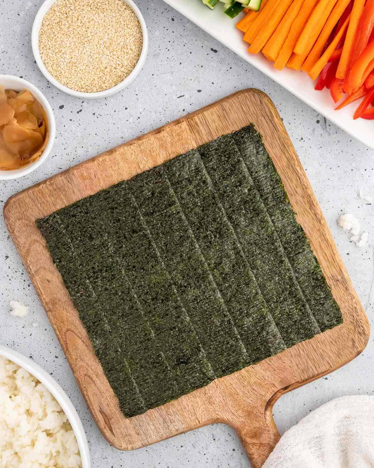 Nori sheet on a cutting board next to chopped veggies for making temaki sushi.