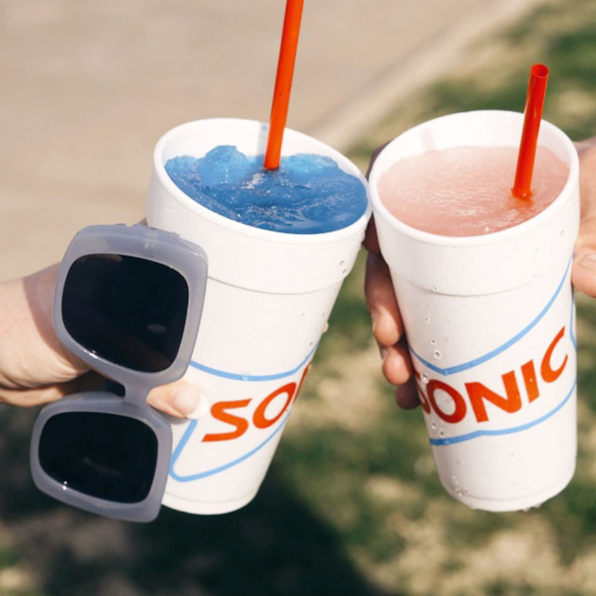 Two hands holding a blue and pink Sonic slushie.