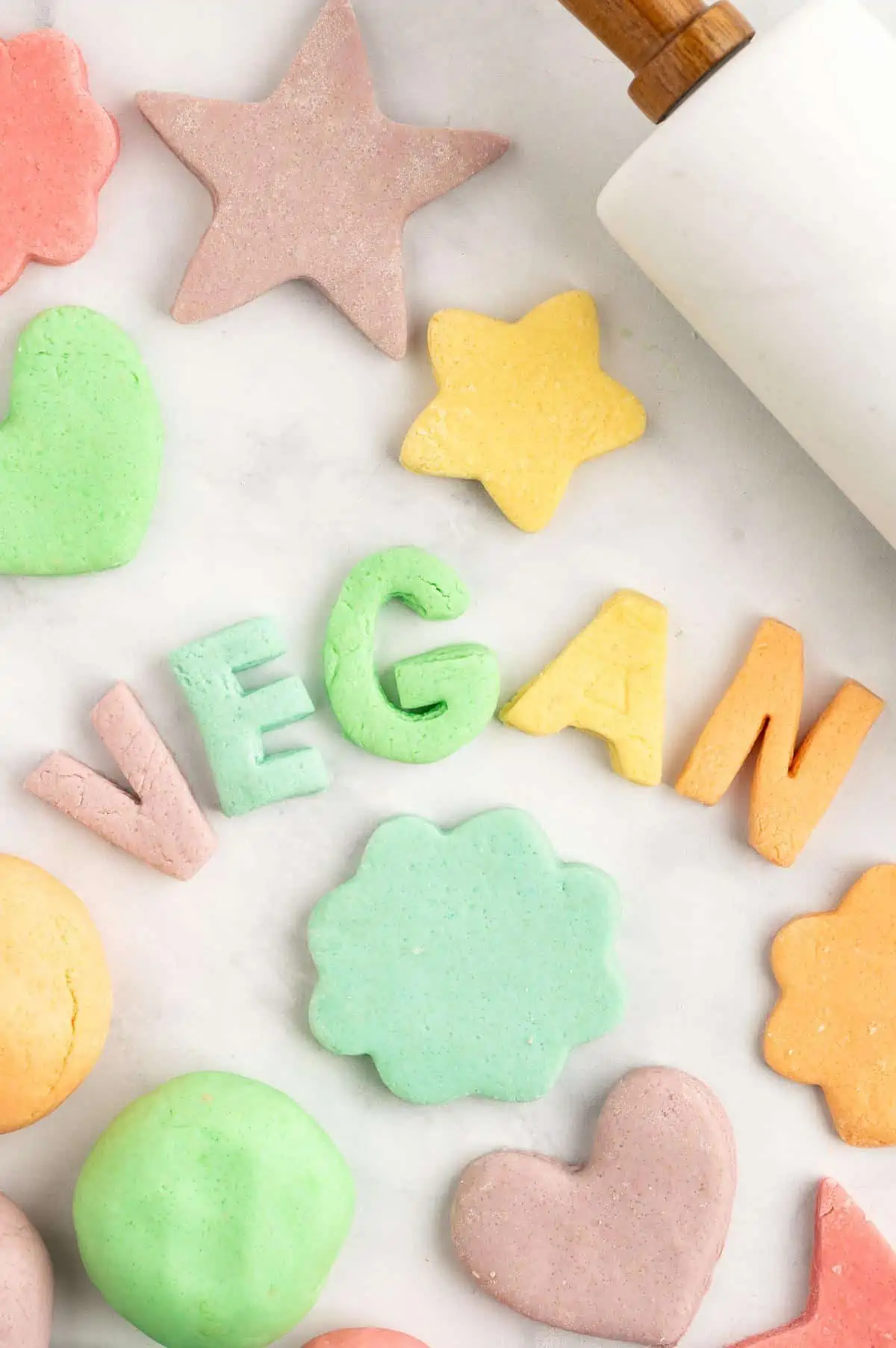 Play dough in different rainbow color, that have been shaped to spell out "vegan" with other stars, hearts and shapes around it.
