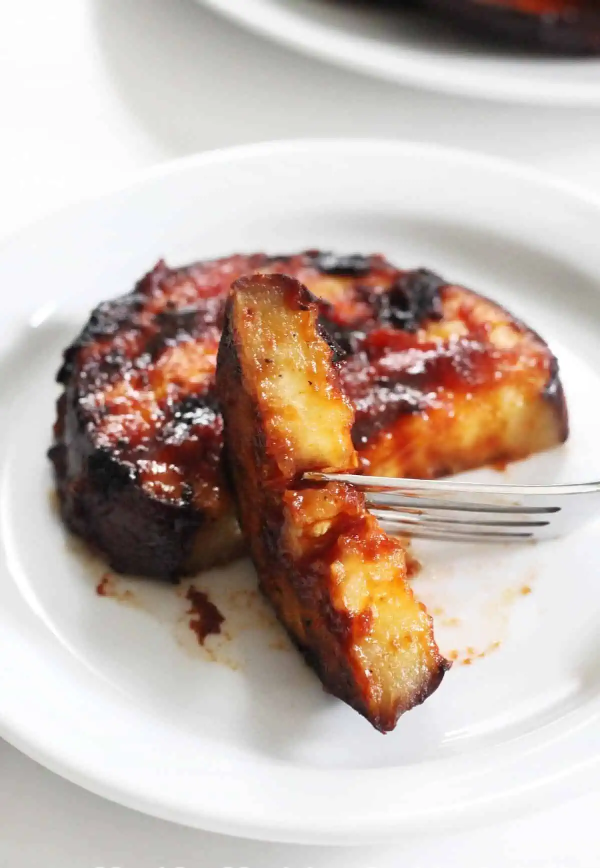 Grilled eggplant steak on a plate with a fork holding a bite that has been sliced off.
