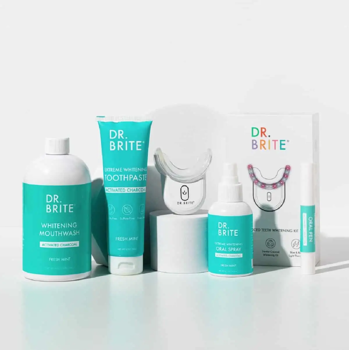 A line up of Dr. Brite oral care items in white and teal tubes and bottles against a white background.