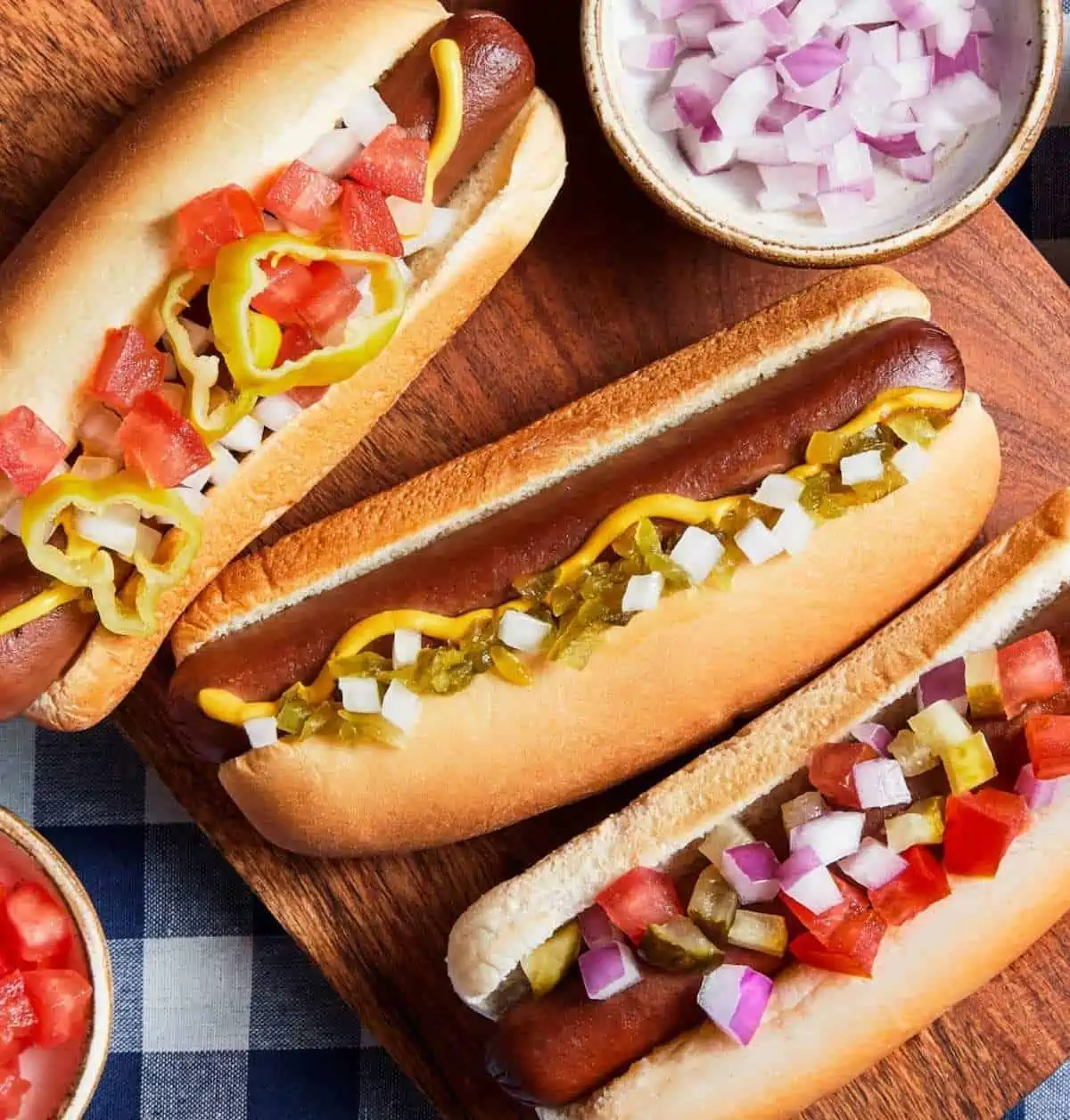 Three Field Roast hot dogs in buns with various toppings.