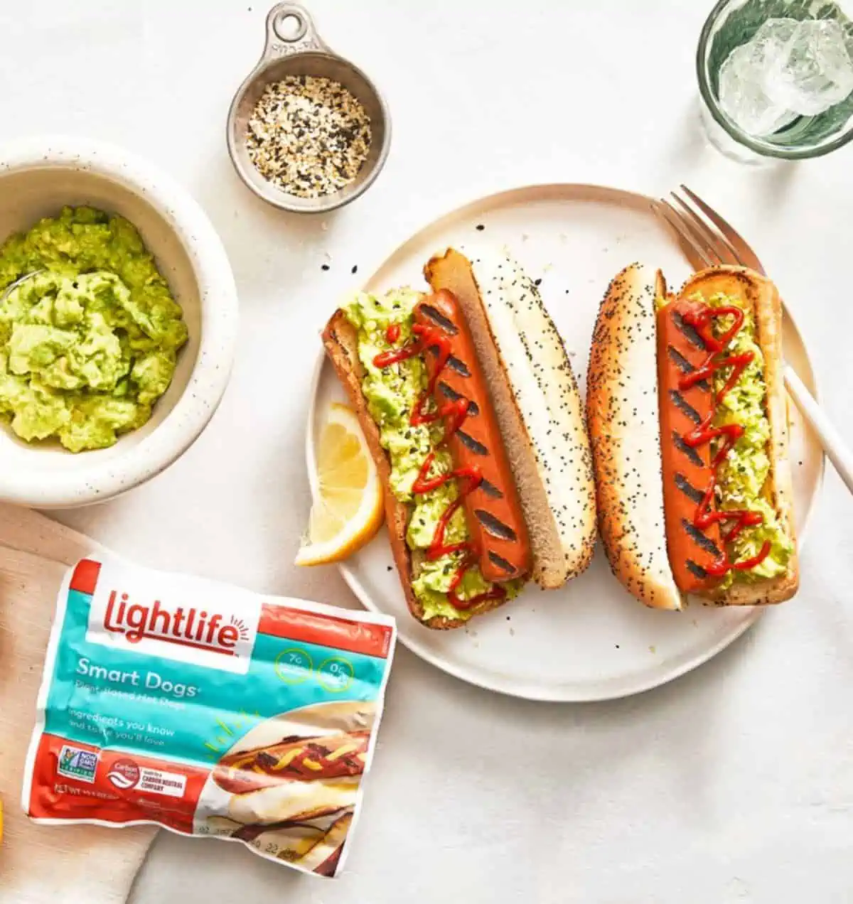A package of Lightlife Smart Dogs next to a plate with two vegan hot dogs in buns topped with guacamole.