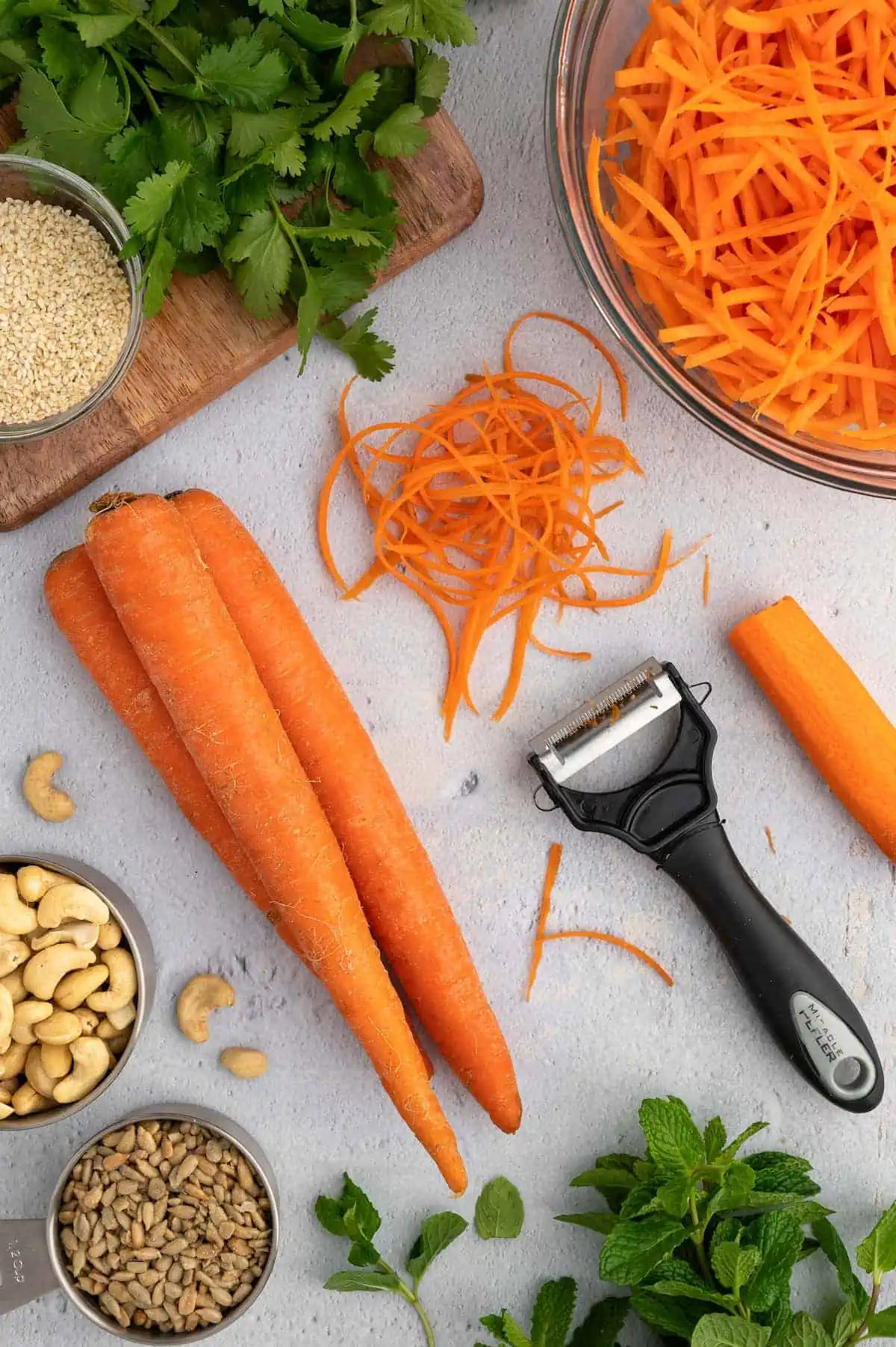 Carrot and carrot shreds, surrounded by produce on a table.