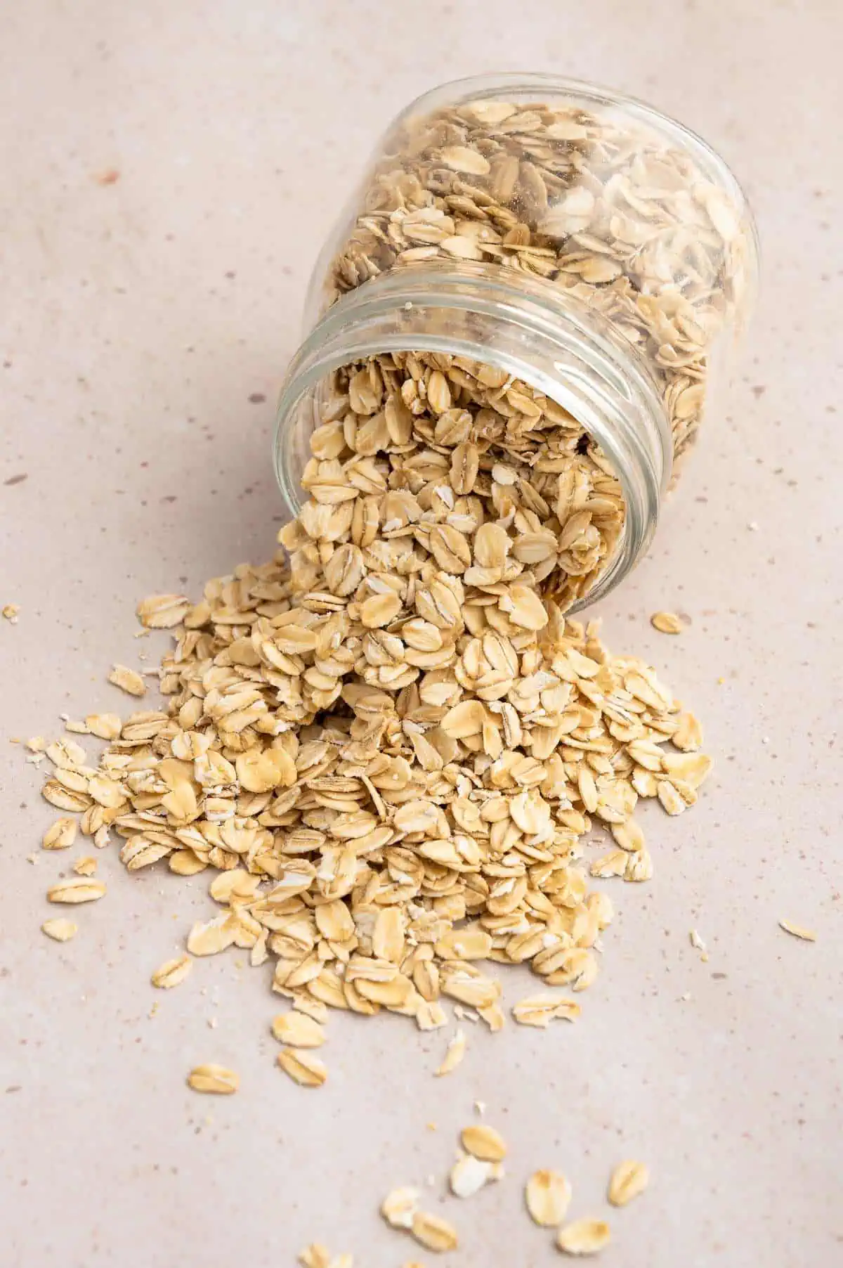 Rolled oats spilling out of a tipped over glass jar.