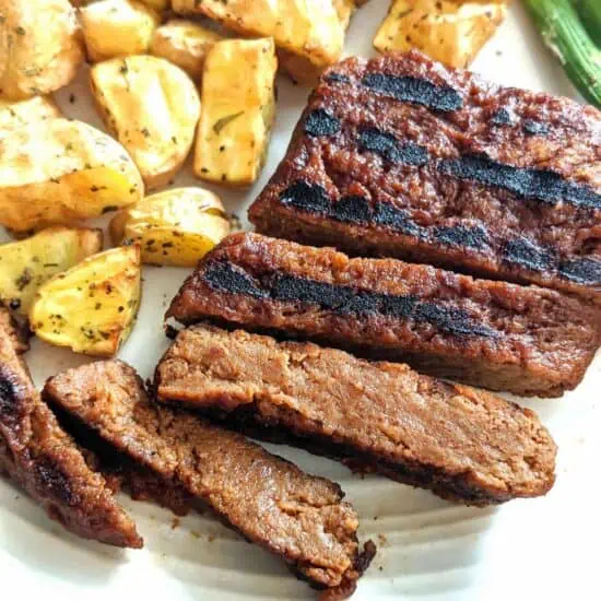 Seitan vegan steak cut into slices, on a plate with potatoes.