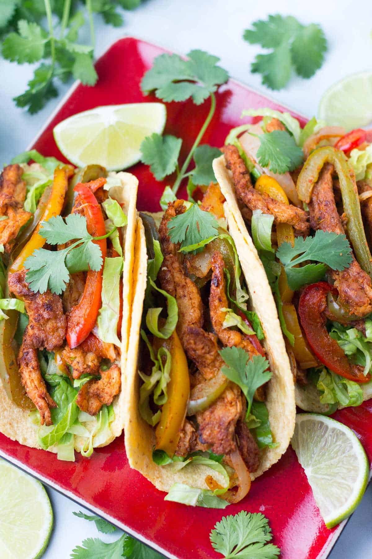 Three soy curl fajitas on a plate topped with fresh cilantro and served with lime slices.