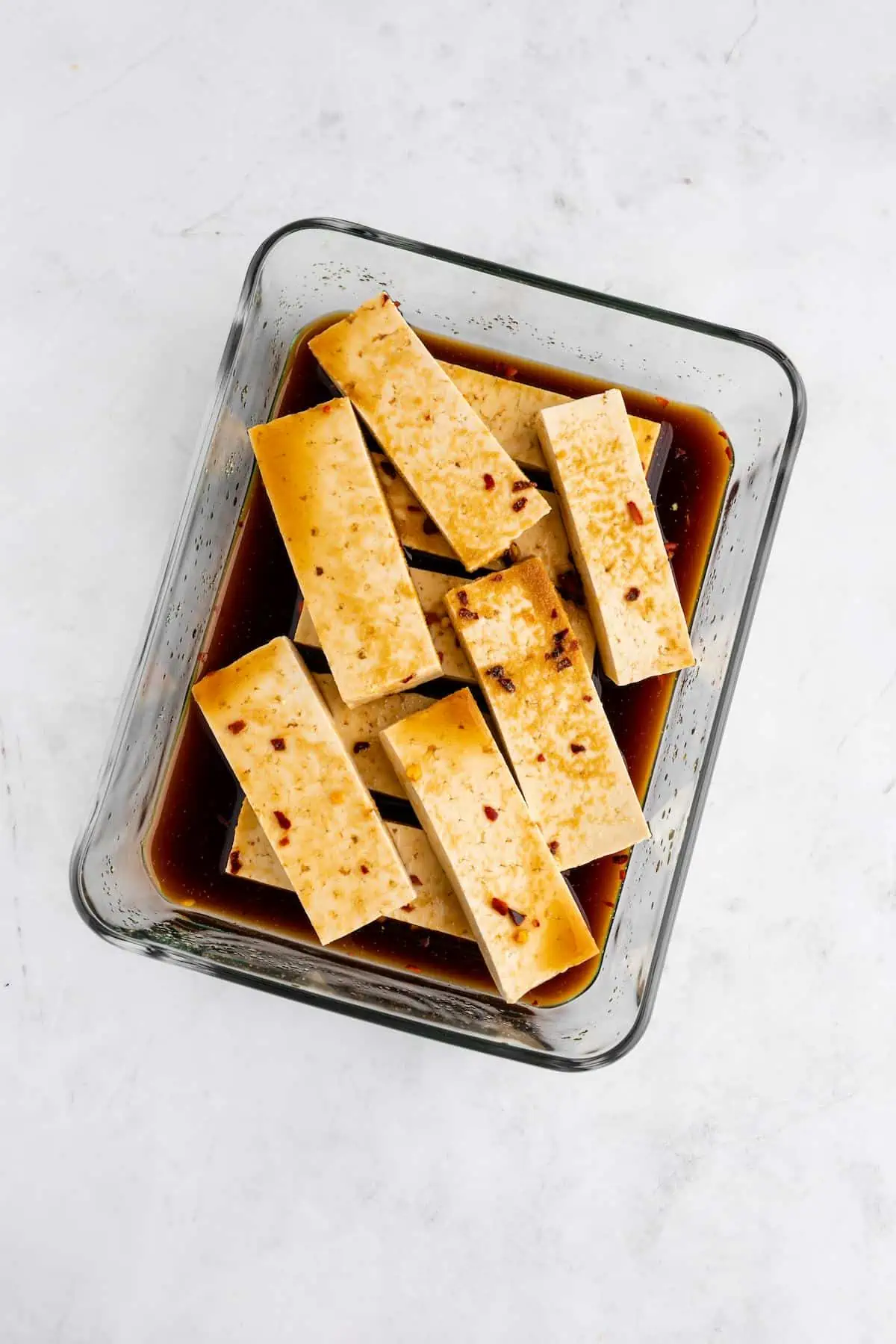 Tofu slices marinating in a large shallow glass dish.