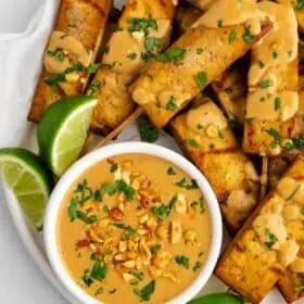 Tofu satay served on a plate with peanut dipping sauce and fresh lime slices.