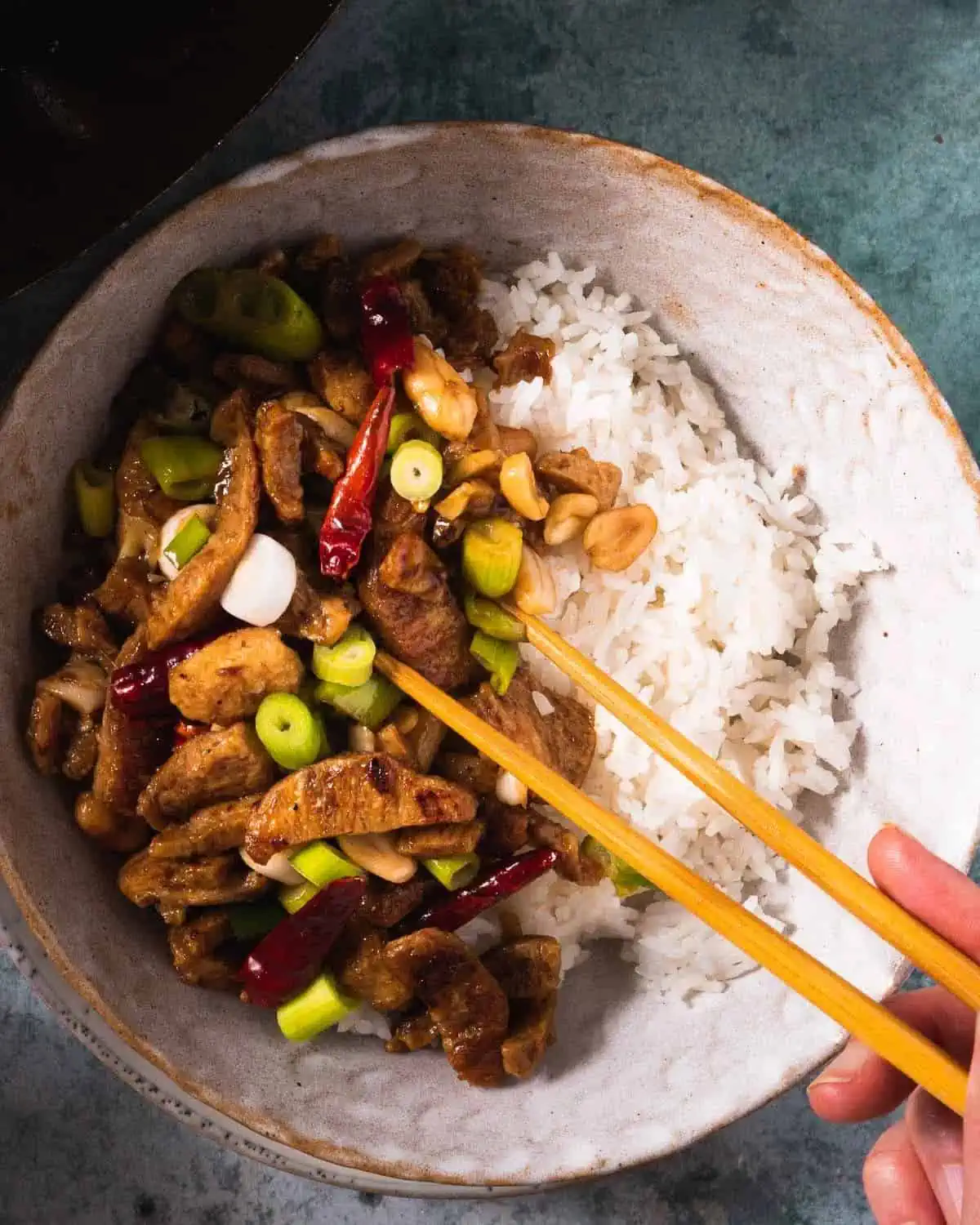 Bowl of vegan kung pao chicken with hand holding chopsticks.