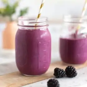 Purple blackberry smoothie in a glass with a paper straw.