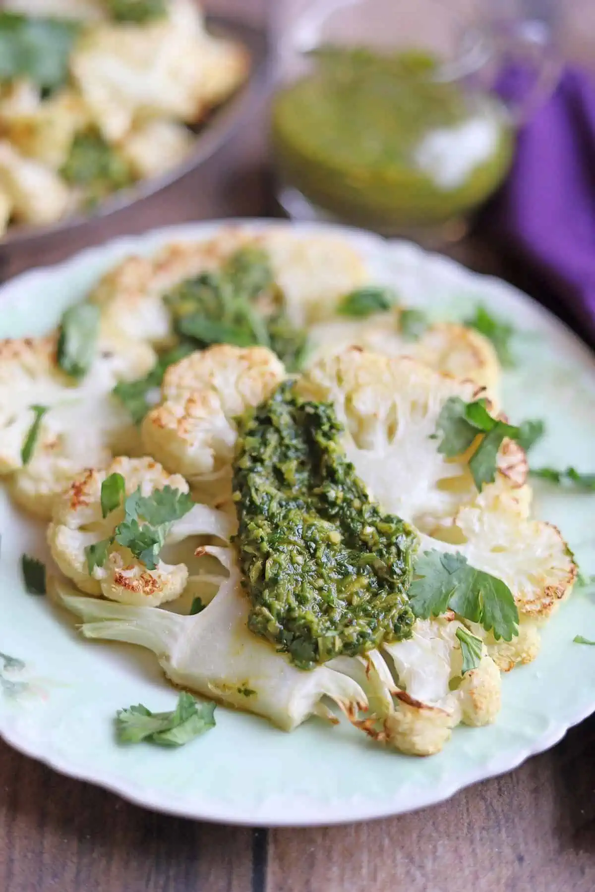 Two cauliflower steaks on a plate topped with chimichurri sauce.