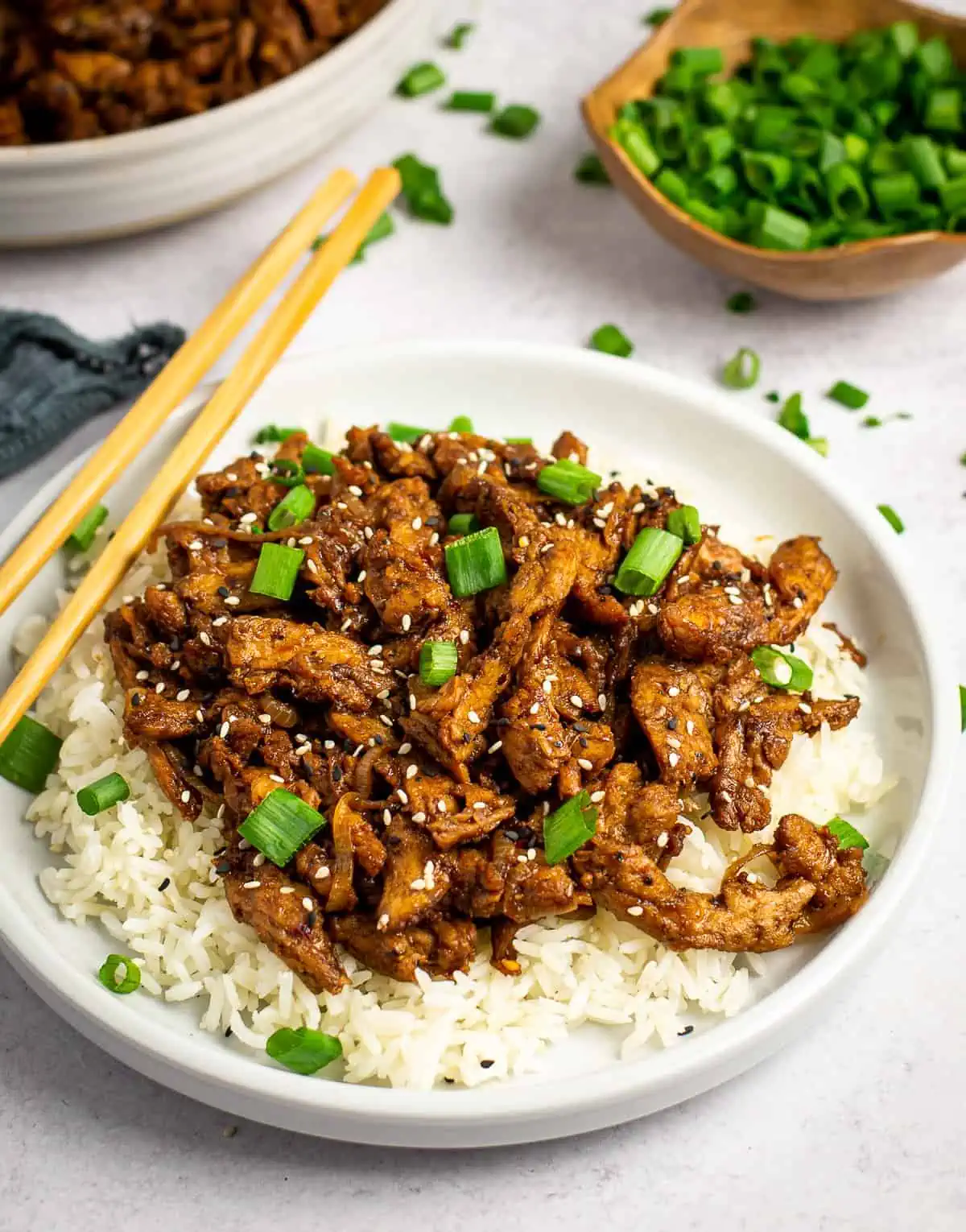 A plate of rice topped with vegan bulgogi, green onion and chopsticks resting on the side.