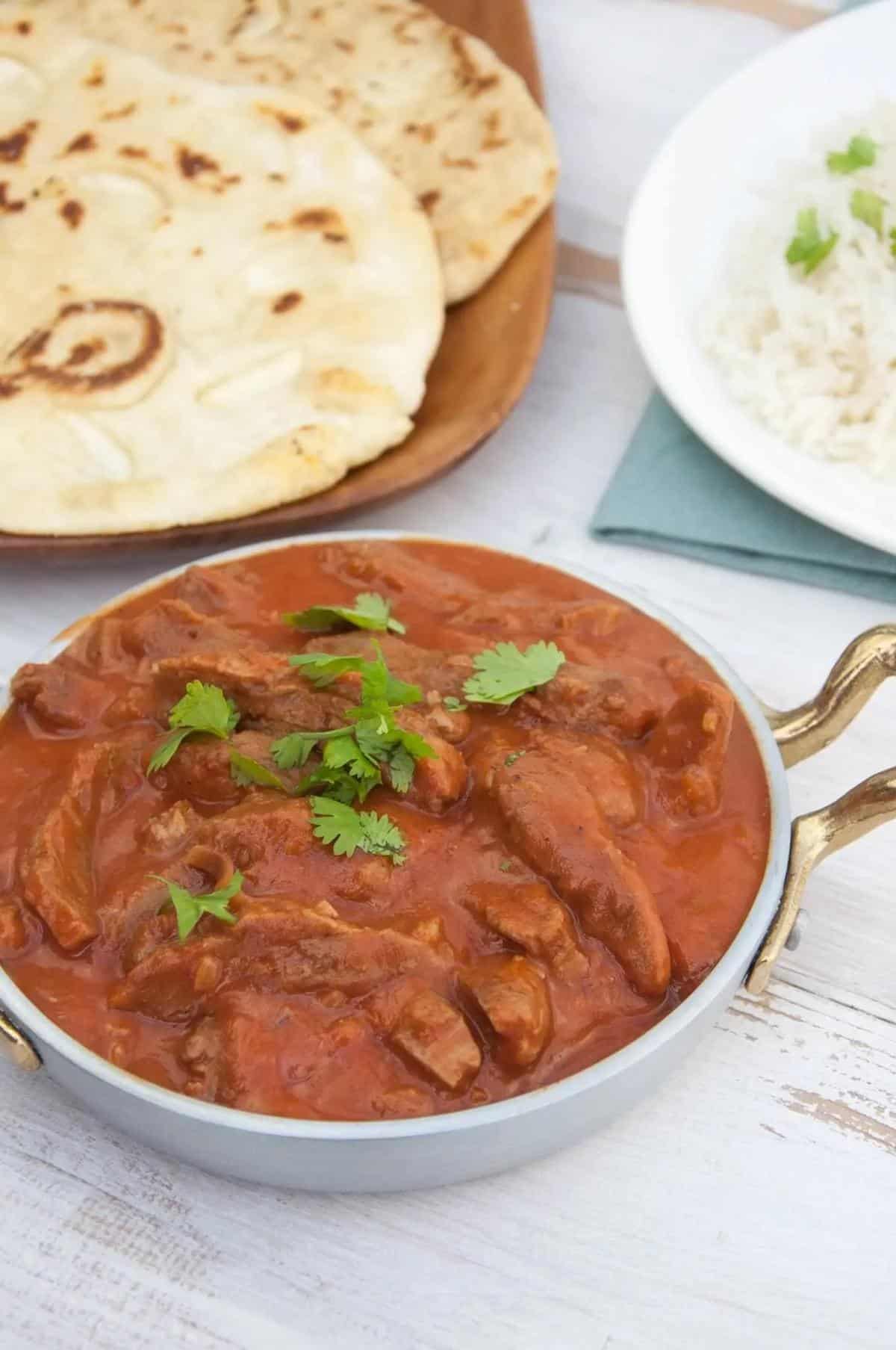 Bowl of vegan butter chicken next to plate of naan.