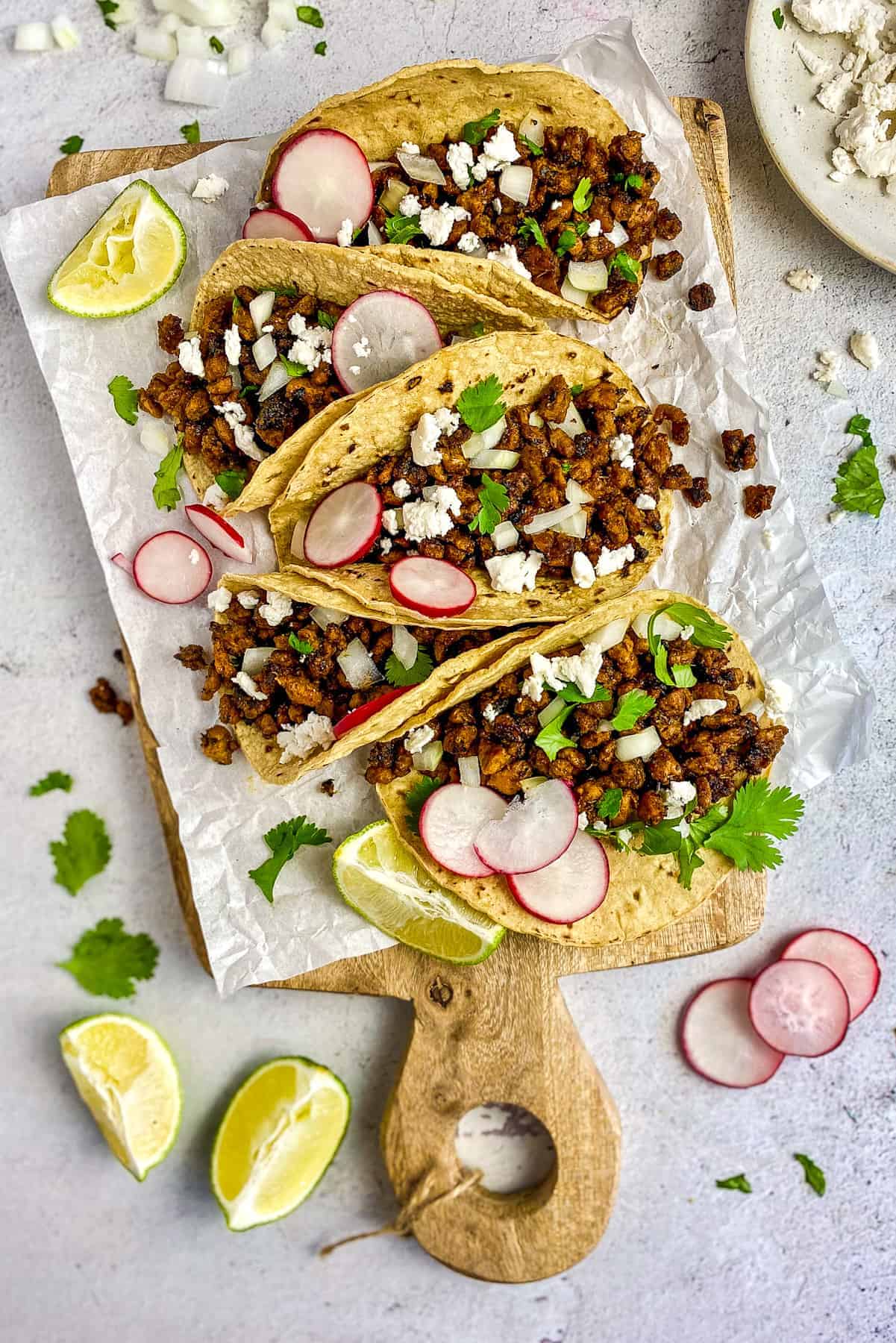 Five vegan tacos filled with vegan carne asada on a platter.