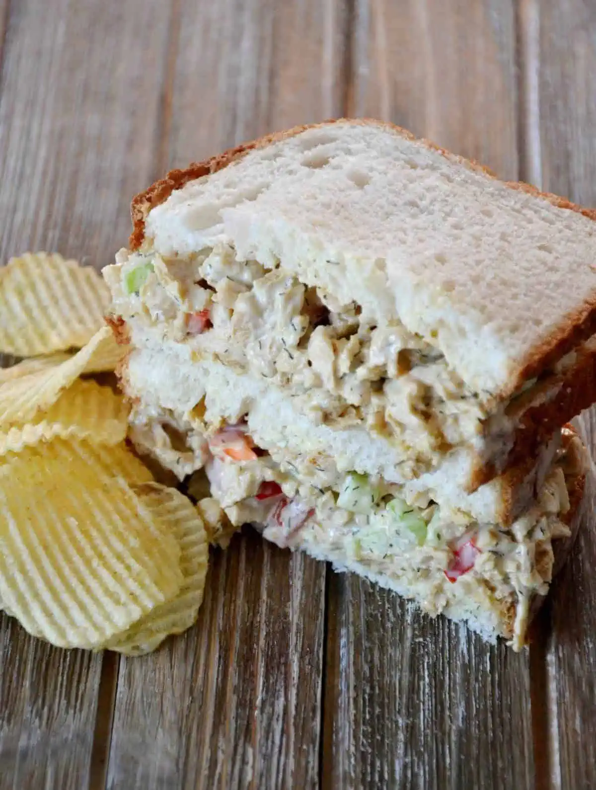 Vegan chicken salad sandwich sliced in half and stacked with cut side facing forward, next to a pile of chips.