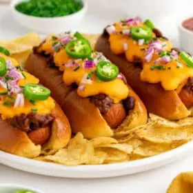 Three vegan chili cheese dogs with plant based cheese served on a plate.