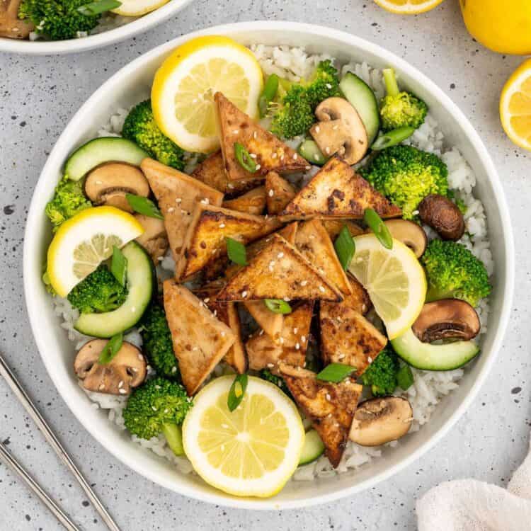 Bowl of golden tofu triangles that have been marinated in an asian tofu marinade and served over rice and veggies.