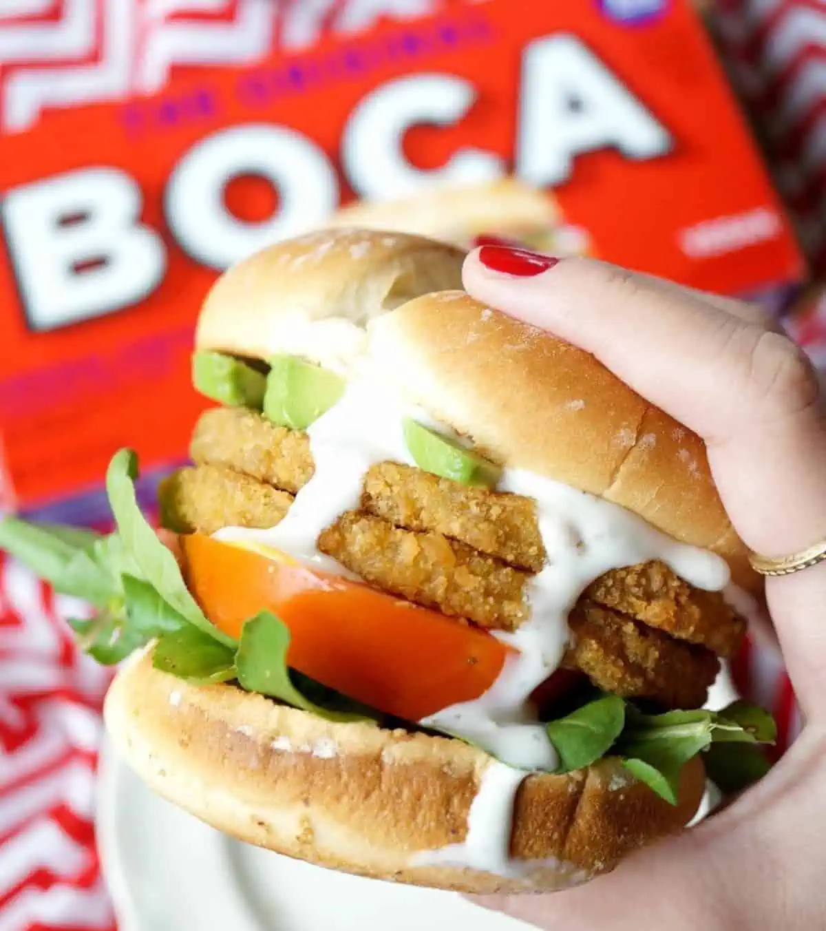 Hand holding vegan burger with two patties, toppings, and dressing dripping down the sides.