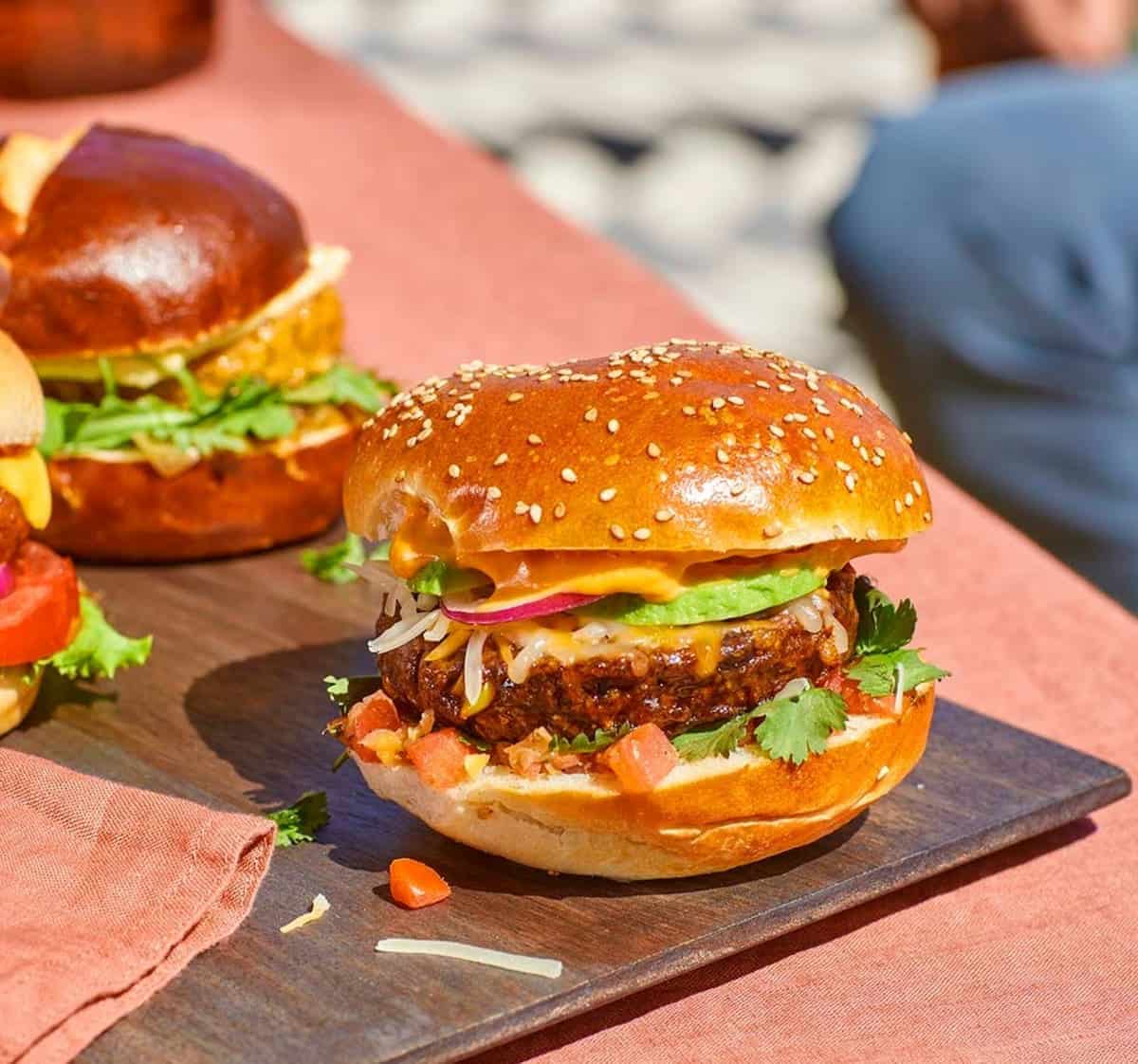 Burgers with all the fixings in a sesame seed bun on a serving board.