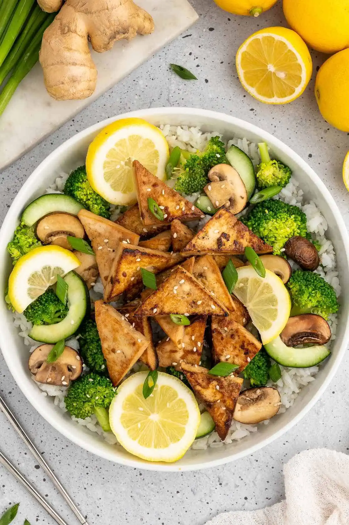 Bowl of golden tofu triangles that have been marinated in an asian tofu marinade and served over rice and veggies.