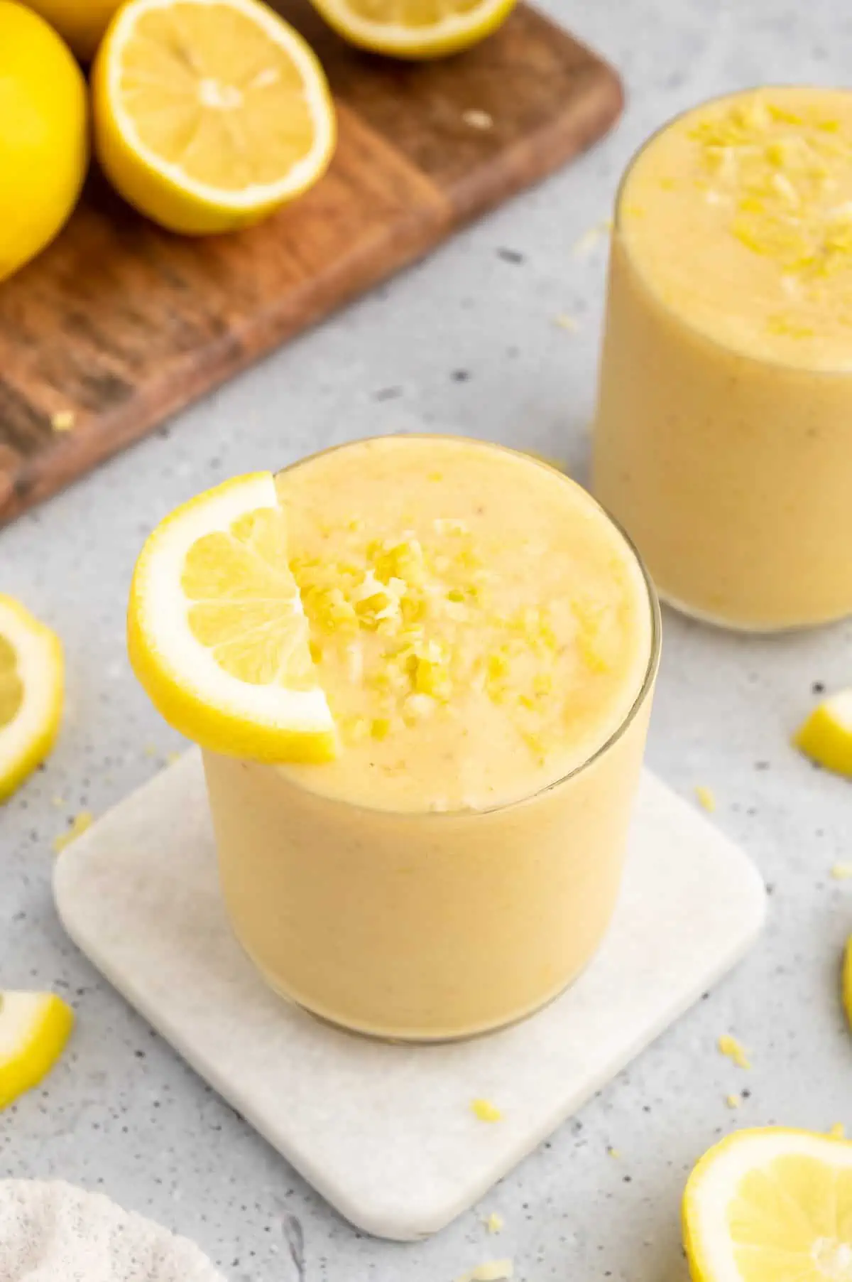 Lemon smoothie in a glass topped with a lemon slice and zest.