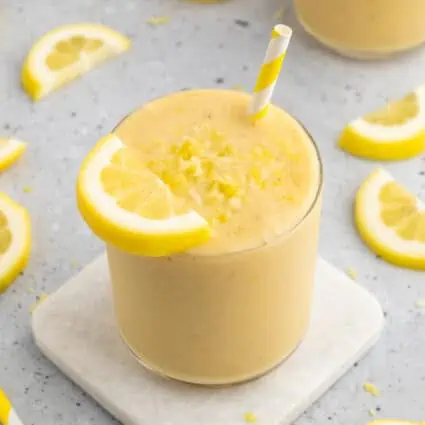 Lemon juice in a small glass with straw and topped with lemon zest and a lemon slice.