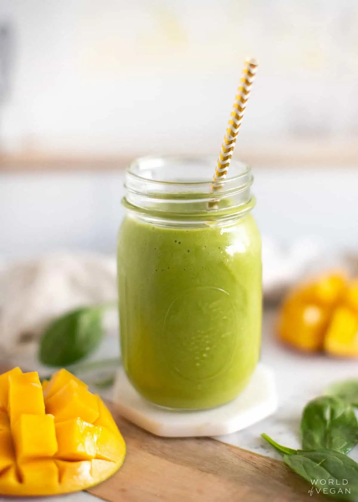A mango spinach smoothie in a glass with a straw.