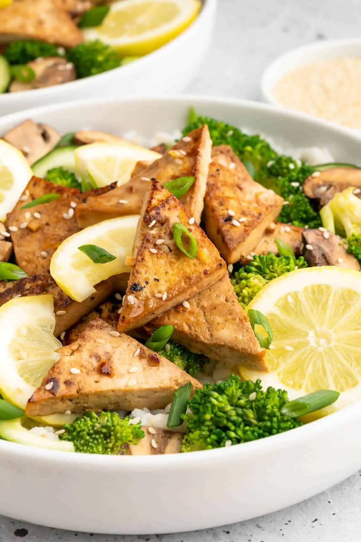 Up close of a bowl of golden tofu triangles that have been marinated in an asian tofu marinade and served over rice and veggies.