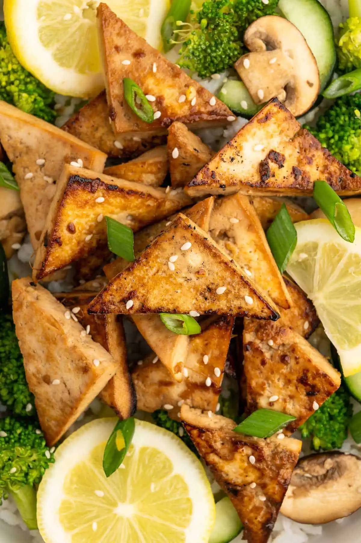 Up close of tofu triangles that have been marinated in an asian tofu marinade and served over rice and veggies.