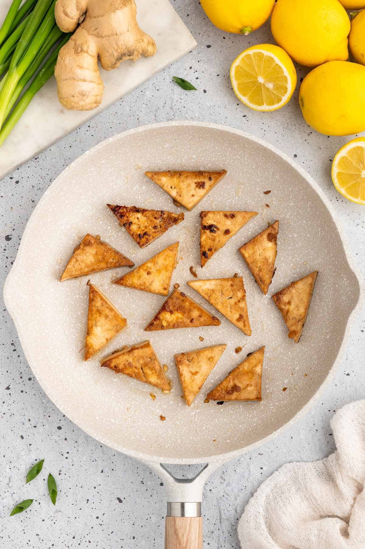 Marinate tofu triangles cooking in a pan.