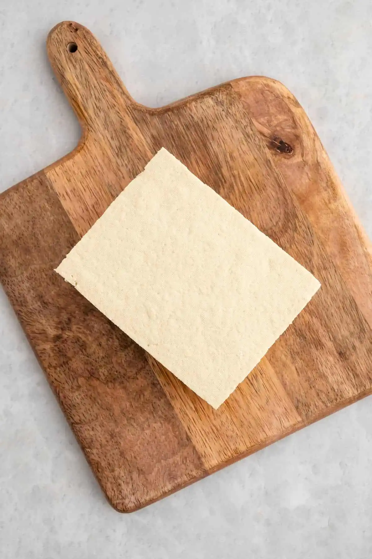 A block of raw tofu on a cutting board.