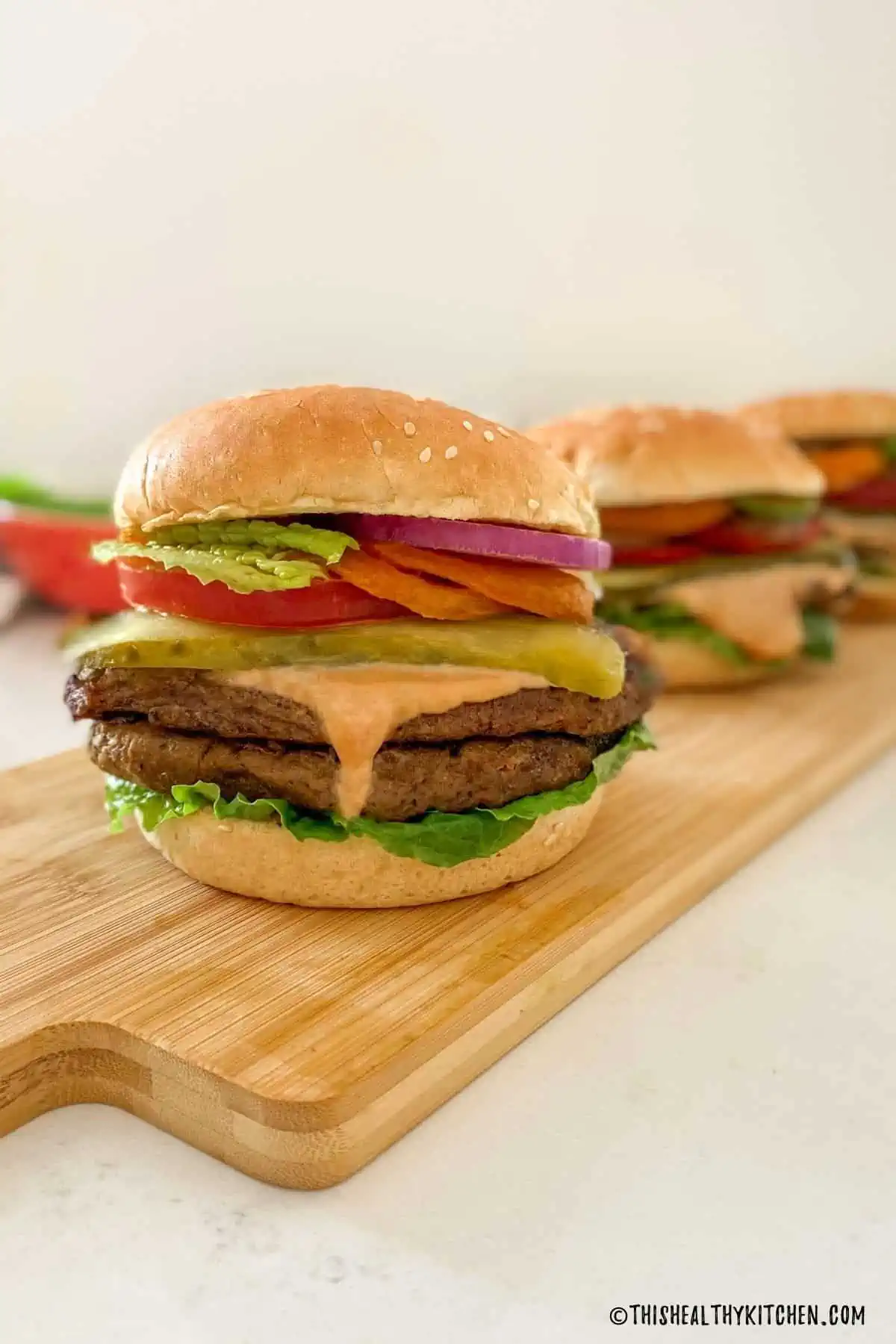 Two seitan burger patties in a bun loaded with toppings.