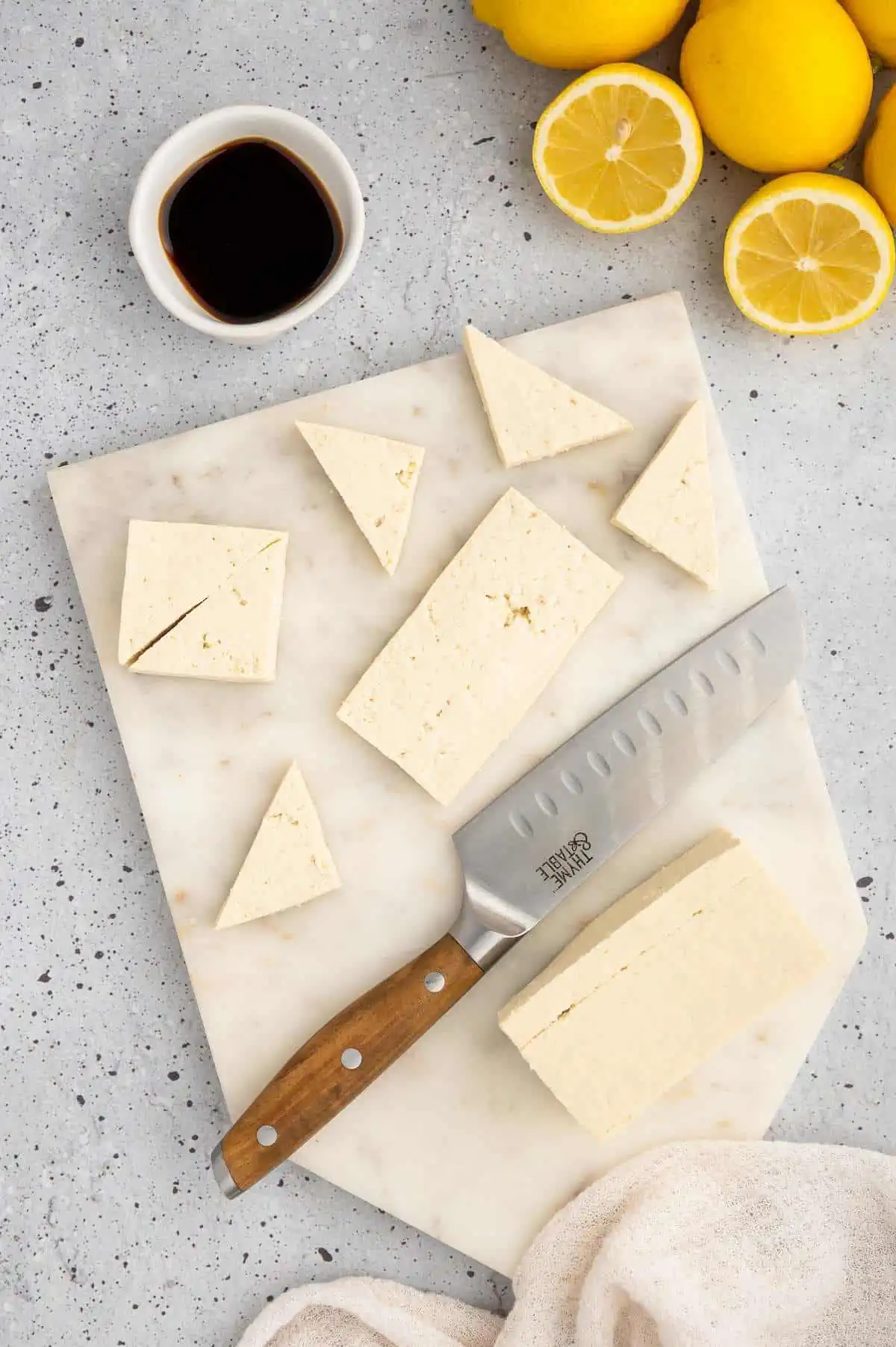 Knife resting on a cutting board next to partially sliced tofu block.