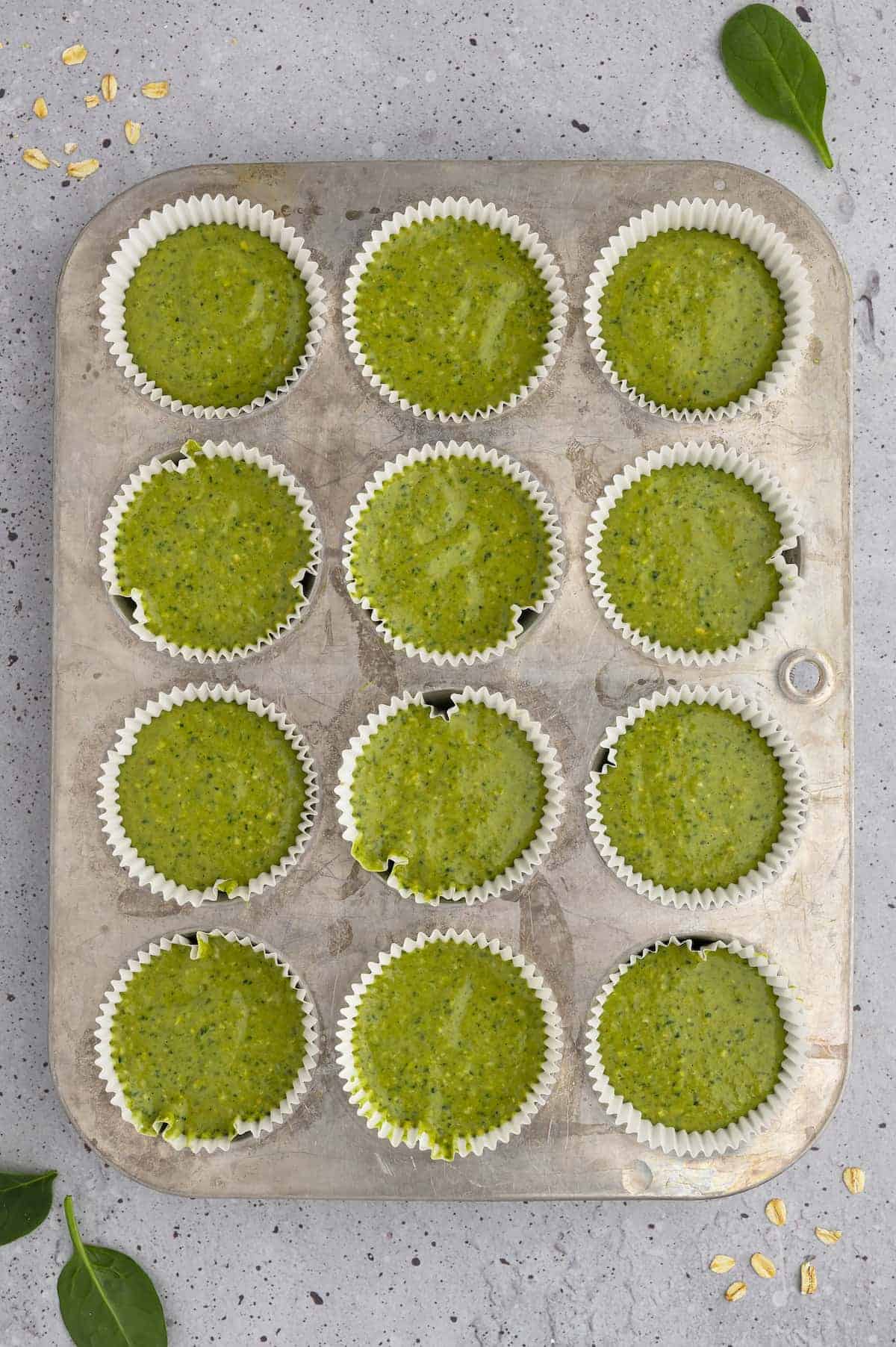 Spinach banana muffin batter in a muffin tin.