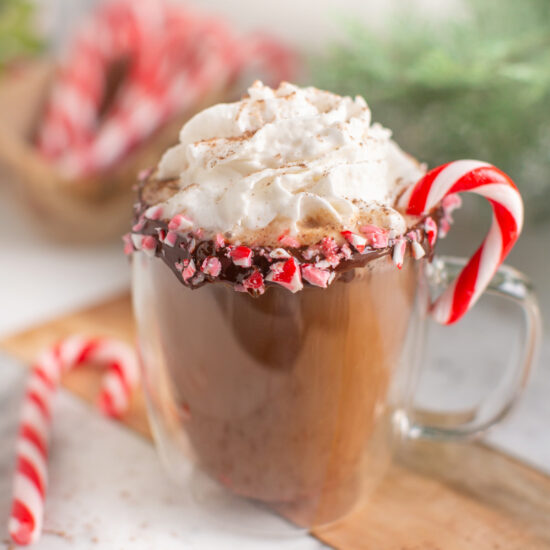 Vegan peppermint mocha in a glass mug served with vegan whipped cream and a candy cane.