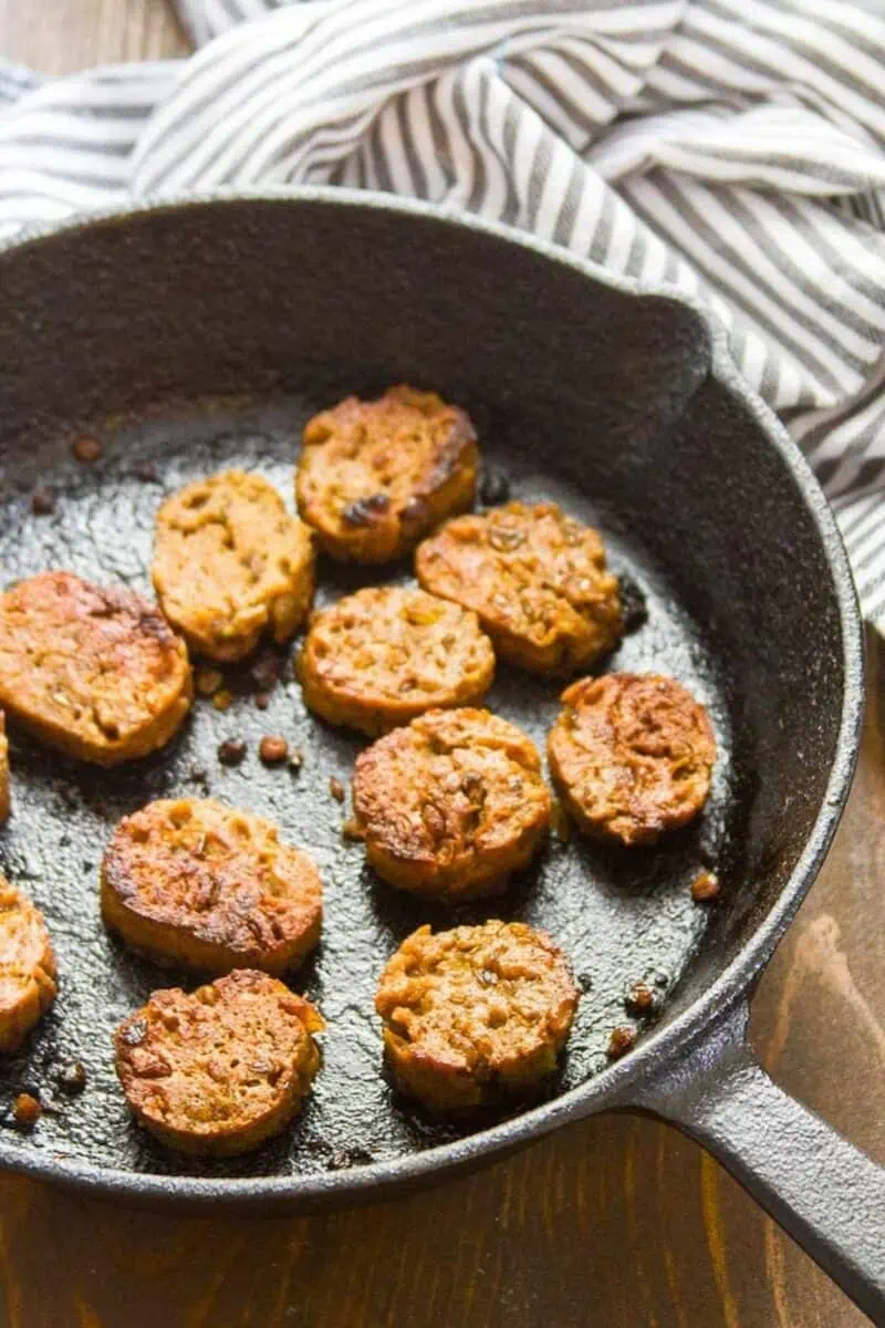 Vegan sausage patties cooking in a cast iron skillet.