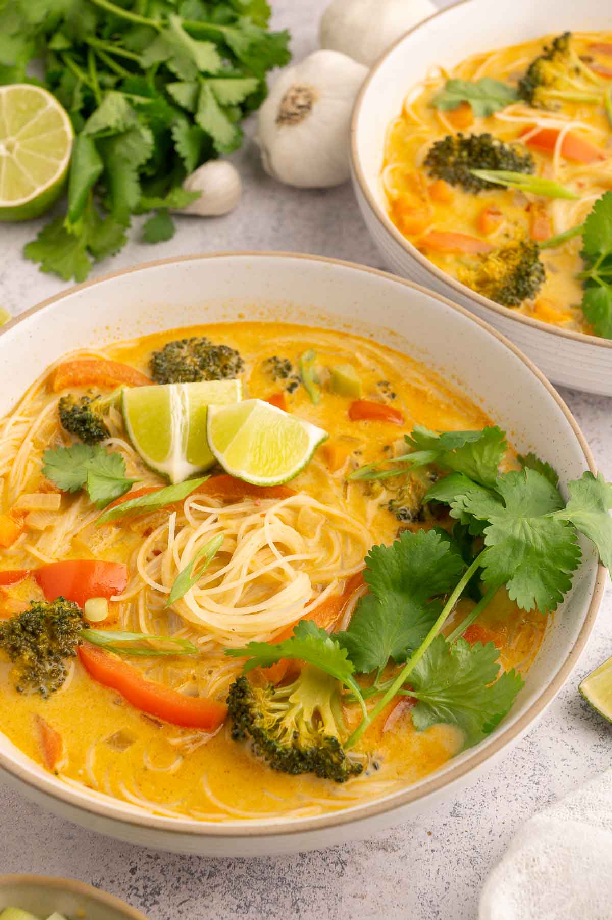 Bowl of vermicelli noodle soup with lime wedges, cilantro, and coconut curry broth.