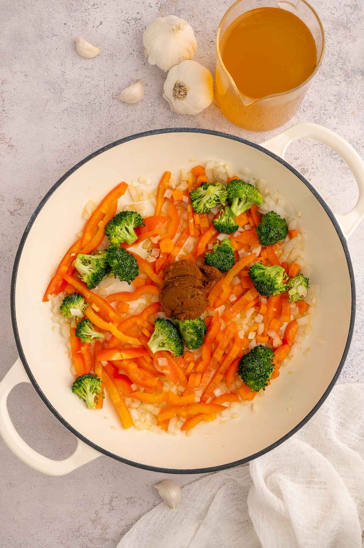 Broccoli, red bell pepper, and yellow curry paste in a pot with sautéed onion and garlic.