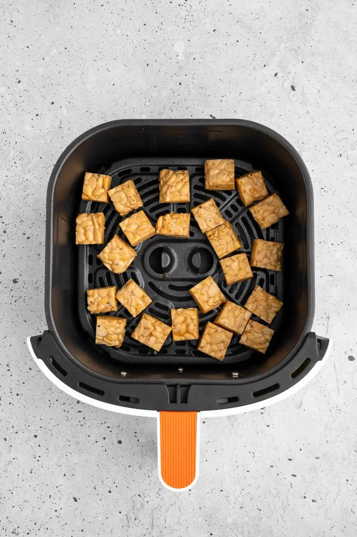 Marinated tempeh in an air fryer basket.