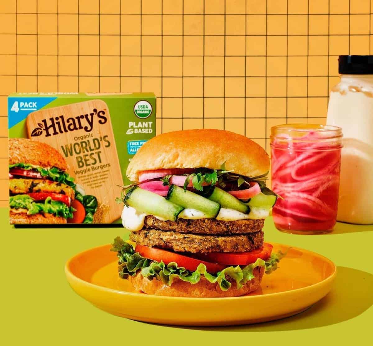 Two Hilary's veggie burgers on a bun, loaded with toppings.