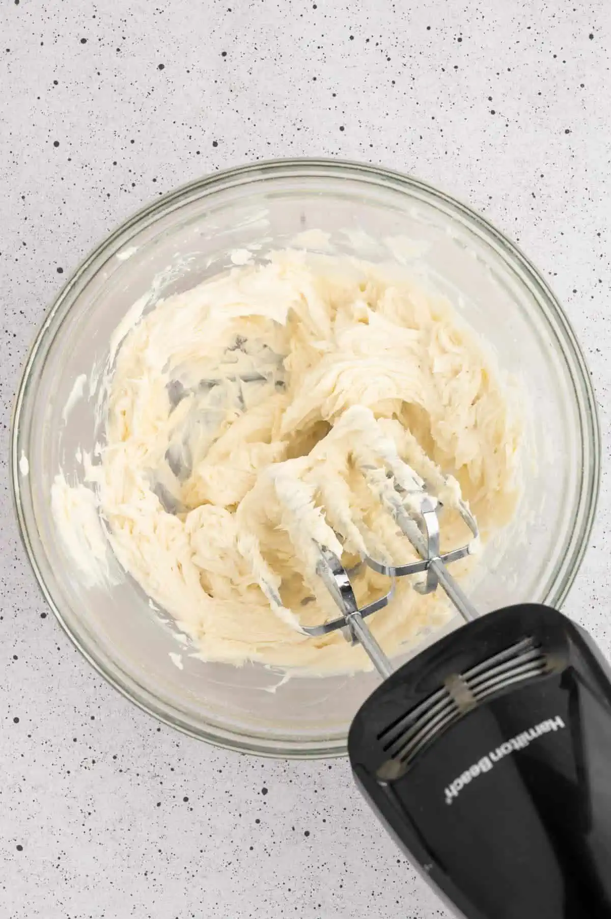 An electric hand mixer whipping vegan butter into vegan buttercream.