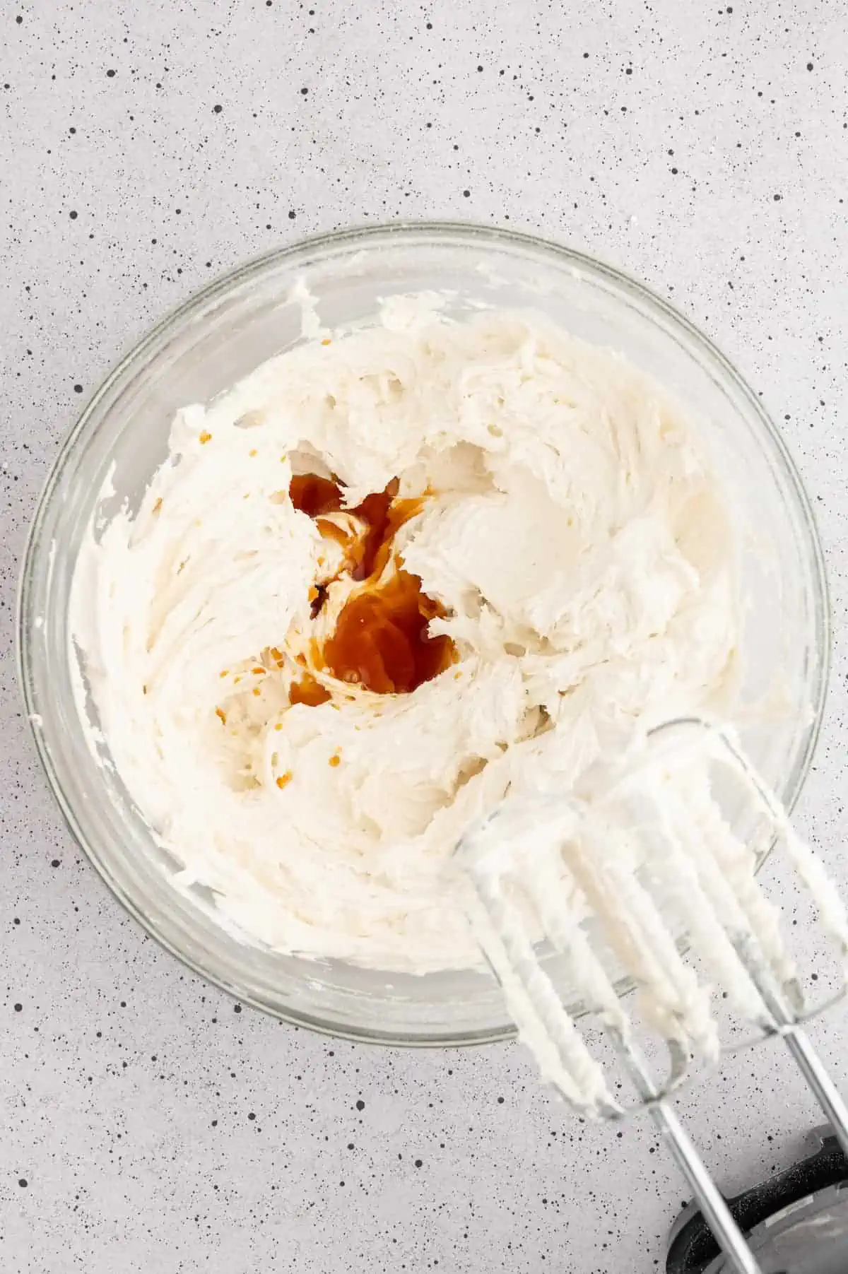 Vegan buttercream with vanilla extract added on top in a mixing bowl.