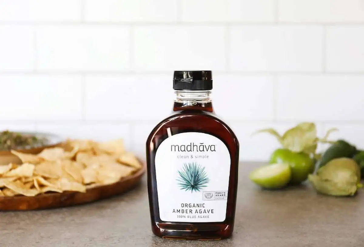 A glass bottle of madhava organic amber agave on a countertop next to chips.
